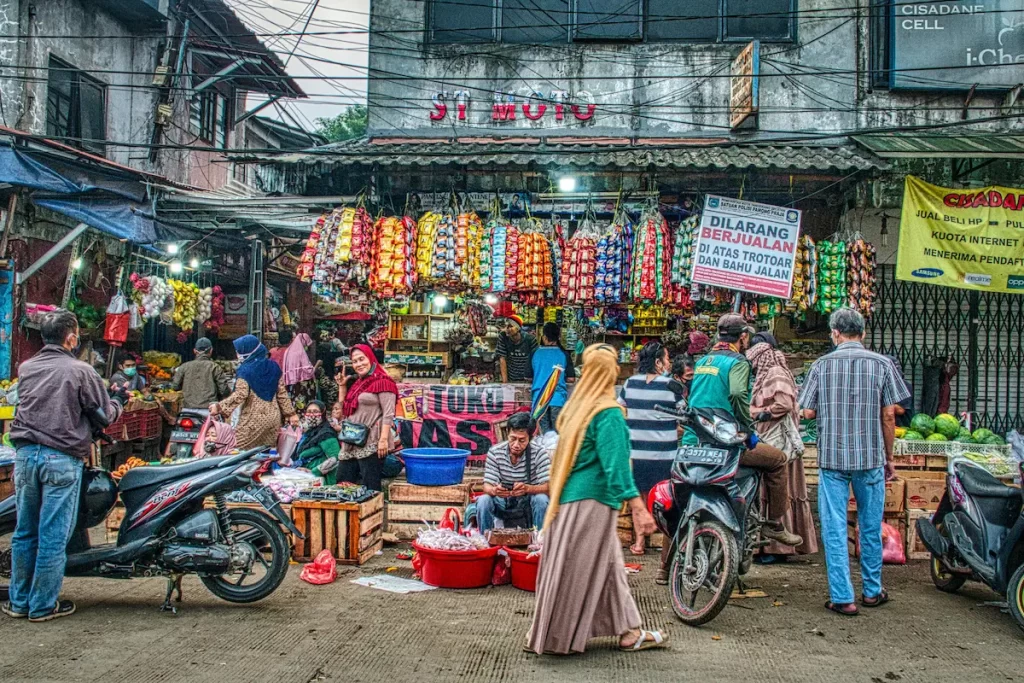 Busy street market scene in Indonesia with stalls, overhead cables, and people moving through the street